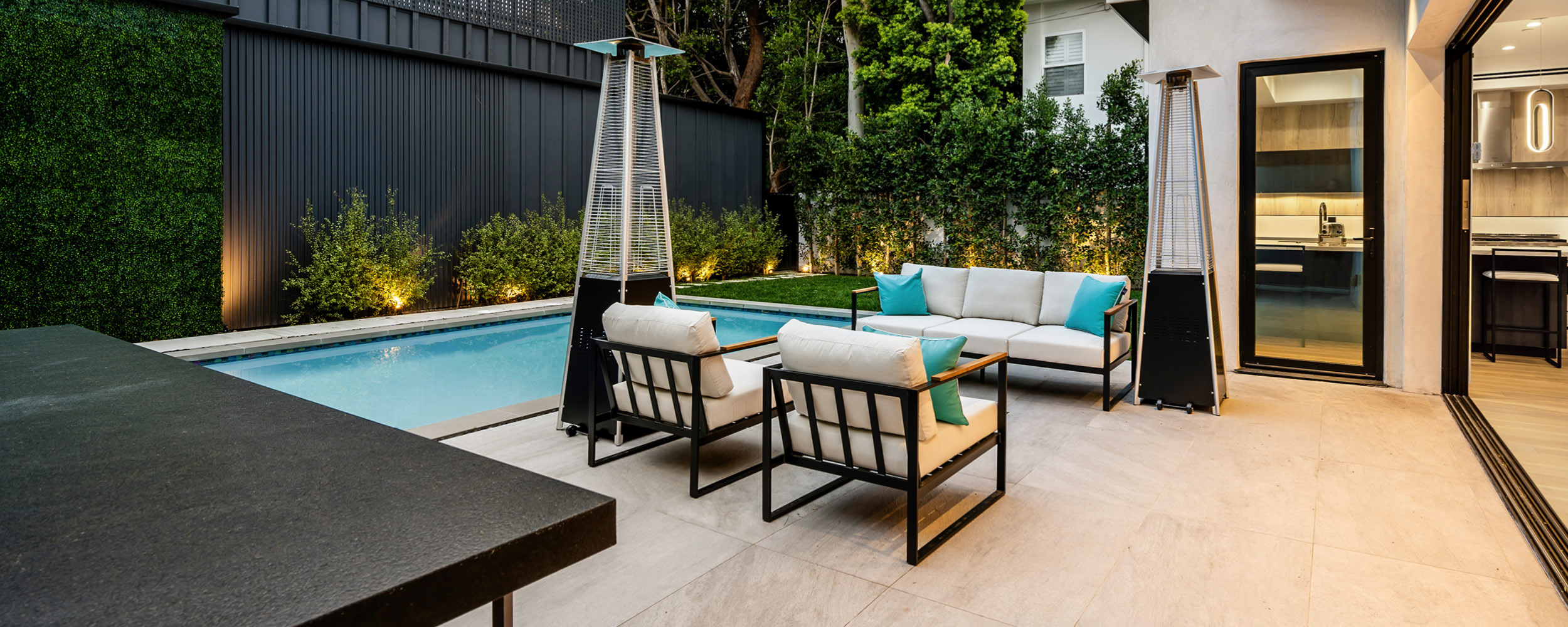 Espace extérieur élégant avec piscine coque moderne, mobilier de jardin confortable et éclairage chaleureux, entouré de végétation luxuriante et revêtement clair, idéal pour détente.