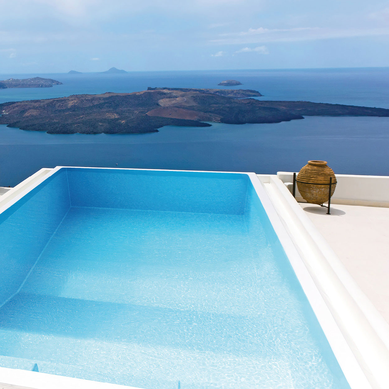 Piscine coque rectangulaire moderne avec vue panoramique sur un paysage maritime, située en hauteur pour une atmosphère luxueuse et relaxante, entourée de décorations extérieures élégantes, idéale pour détente estivale.