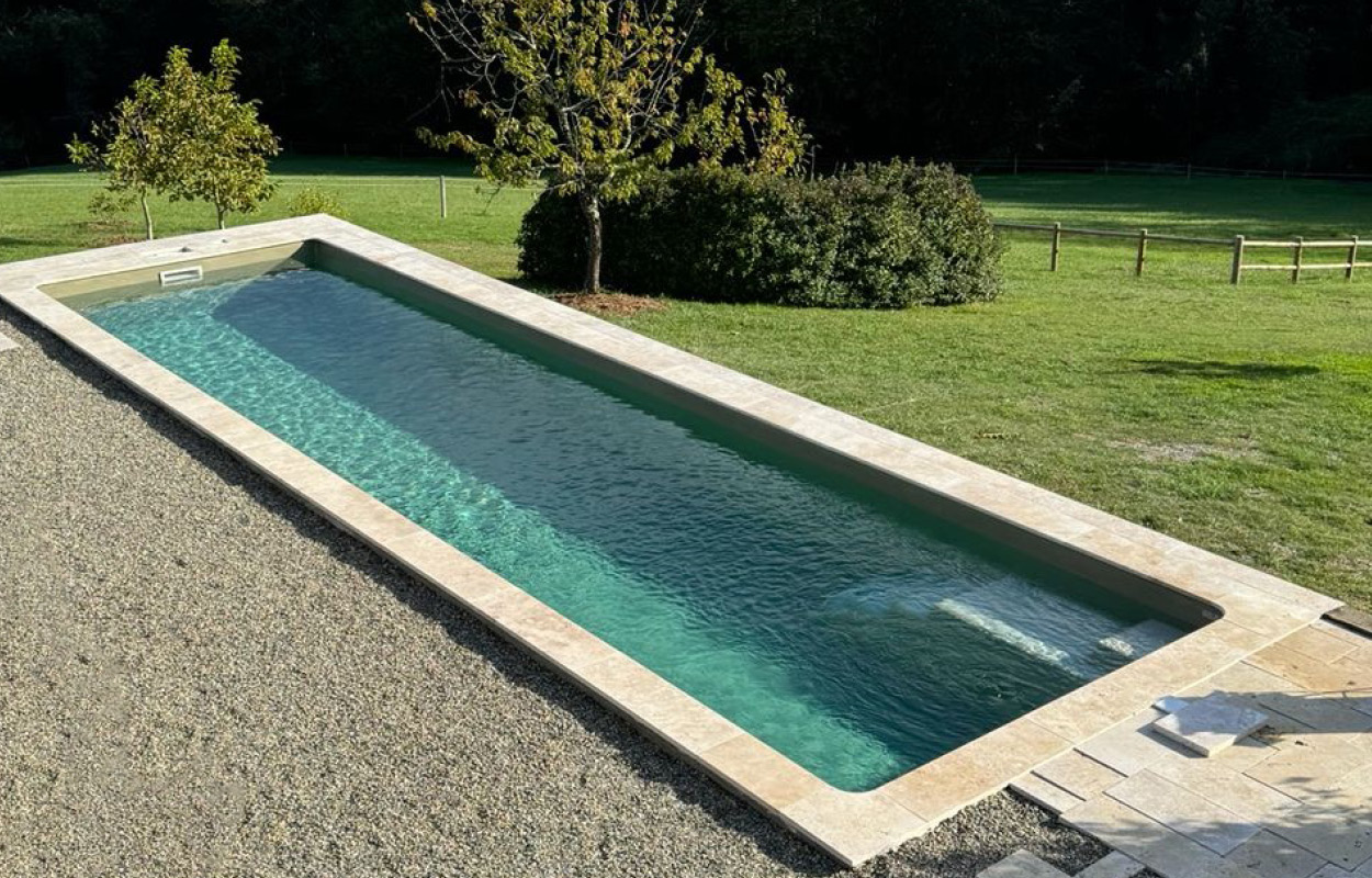 Piscine coque moderne et spacieuse au design contemporain intégrée dans un environnement verdoyant avec eau claire et cadre naturel, idéale pour un jardin esthétique.