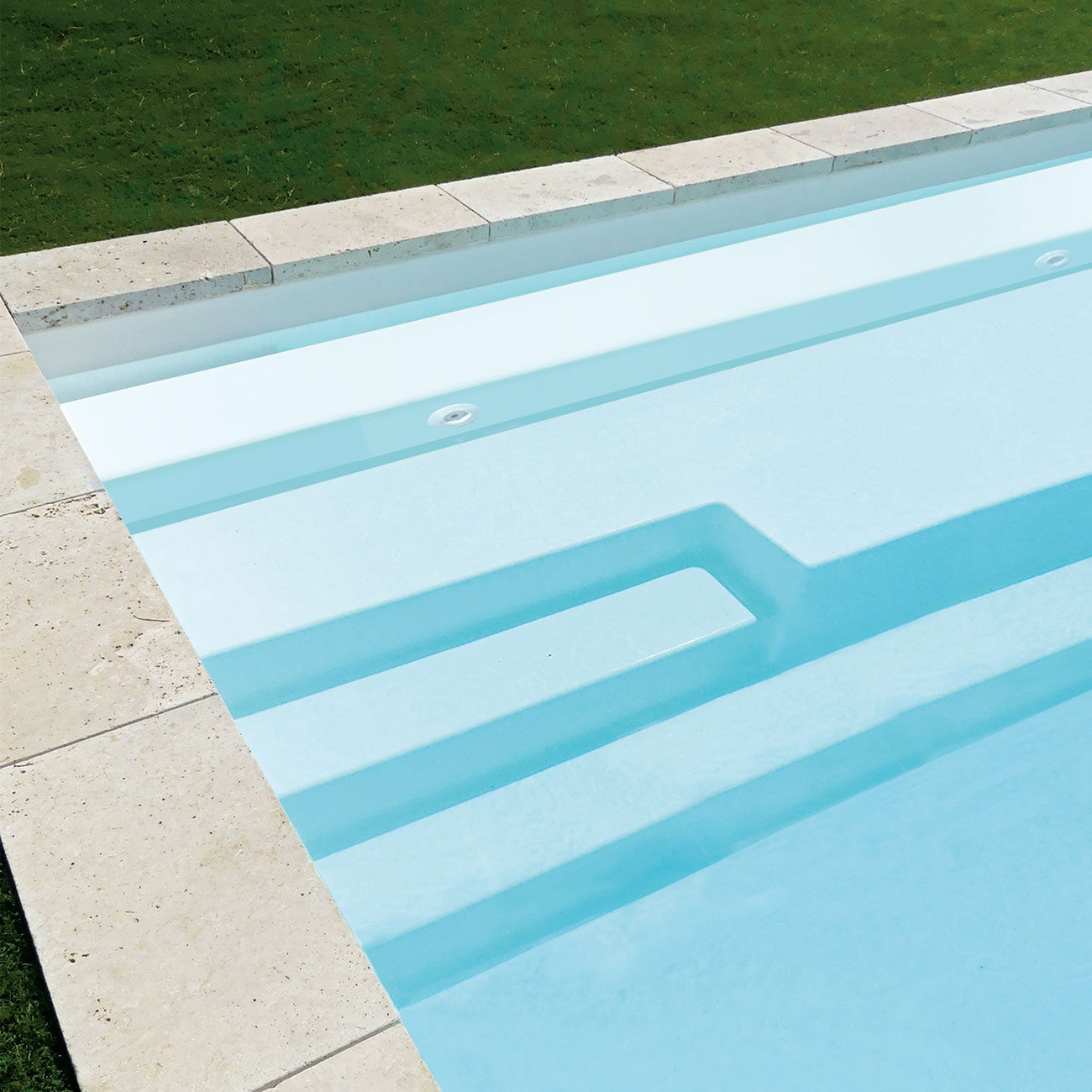 Piscine coque moderne avec lignes épurées, surface bleu clair et éclairage encastré, entourée d'un revêtement en pierre dans un jardin soigné.